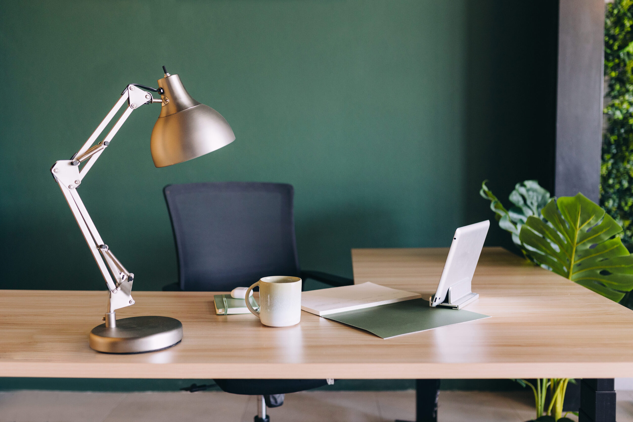 Home office desk setup with lamp, laptop, coffee mug, and a green wall in the background.