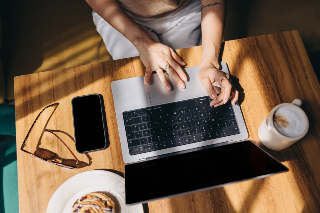 Overhead picture of a person sitting at a table with a laptop, phone, glasses, and cup of coffee.