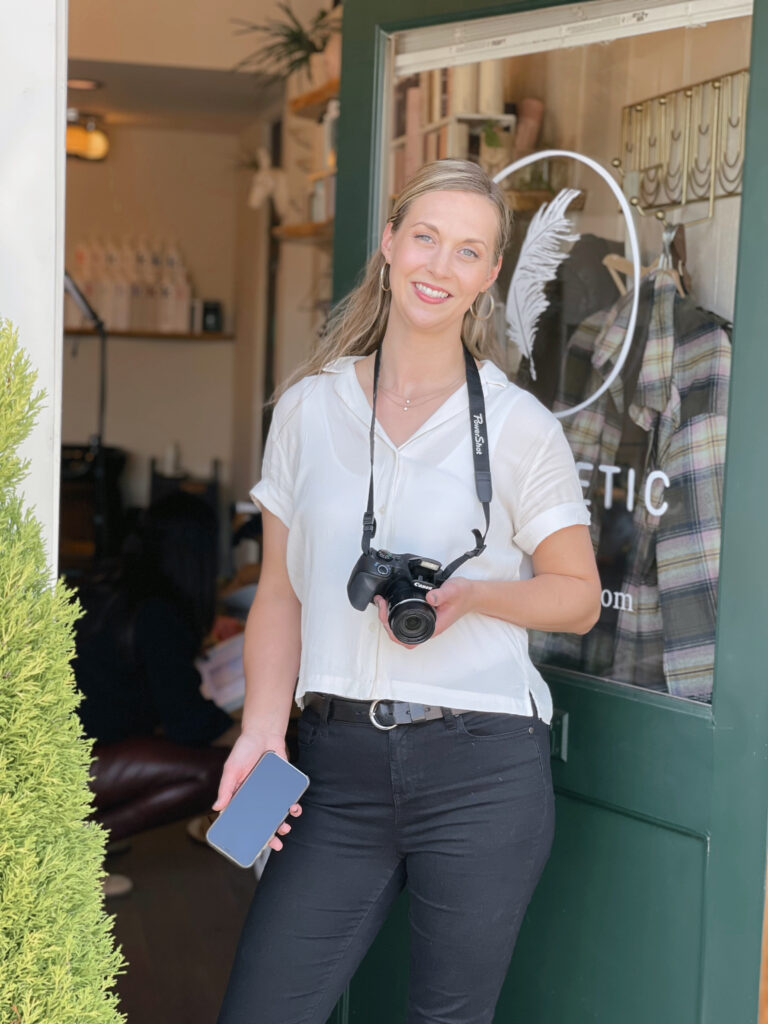 Blonde woman standing in a doorway with a camera and phone in her hand.