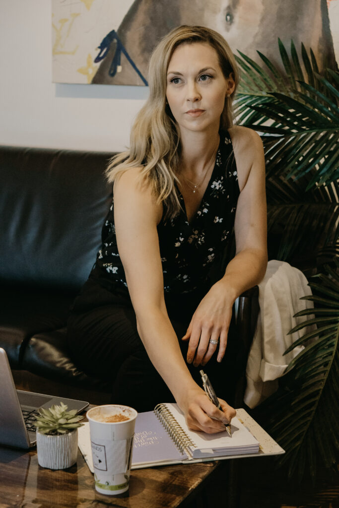 A blonde woman sitting on a black couch while writing in a daily planner.