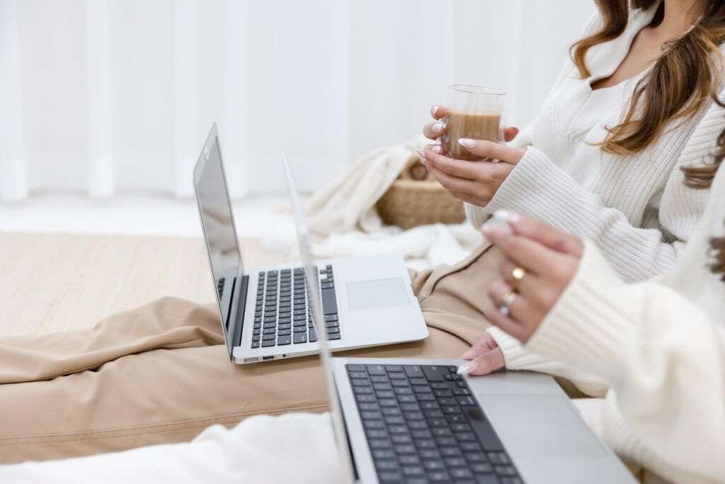 Close up of two people sitting with laptops on their legs and one holding a coffee cup.